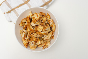 fried chicken pieces in white bowl. Dinner on white table. Close-up, copy space, top view