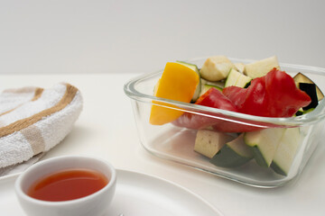 On a white table there is a bowl with fried chicken, a baking tray with vegetables and a plate with a fork. Homemade dinner on a white background. Copy space