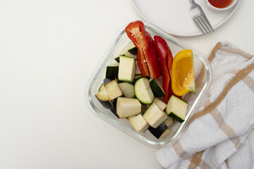 On a white table there is a bowl with fried chicken, a baking tray with vegetables and a plate with a fork. Homemade dinner on a white background. Copy space