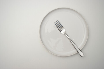 White plate on a white table. There is a fork on the plate. Top view, copy space