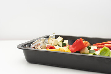 On a white table there is a metal baking tray with vegetables. Close-up, copy space. Zucchini, bell pepper and eggplants for baking.