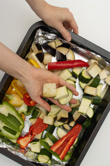 Female hands put vegetables in a baking tray. Eggplant, zucchini and bell pepper in the oven. Homemade dinner. Close-up, copy space