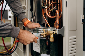 Technician's hands with tools working on the copper pipes of the air conditioner. The photo shows...