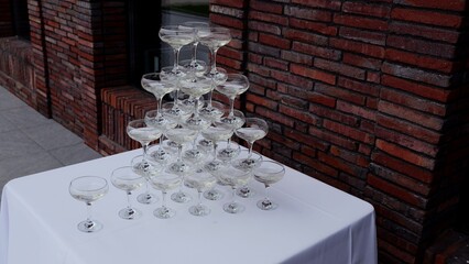 Champagne glass pyramid balancing elegantly on white draped table, brick wall background suggesting...