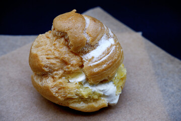 Choux cream placed on brown paper with black background. Close-up choux cream or cream puff texture. Dessert, baked goods, vanilla, and homemade pastry concepts. Dessert setting on black background.