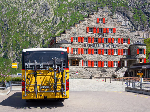 Grimselpass, Switzerland - August 8, 2024: Hotel Grimsel Hospiz is a historic hotel located in the Swiss Alps. Yellow post bus transporting bicycles in front of the building