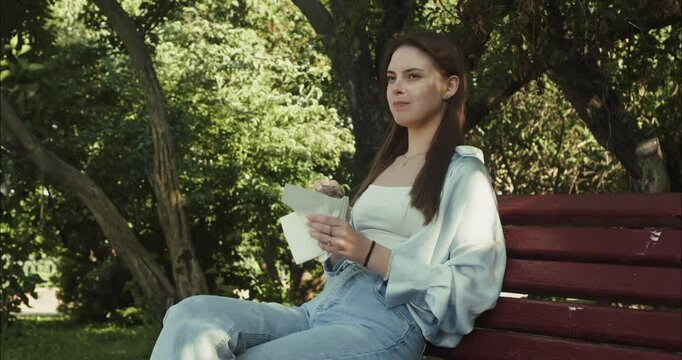 Young woman enjoying a snack on park bench