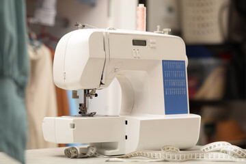 One sewing machine with thread and measuring tape on white table in workshop