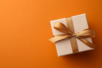 Beautiful gift box with golden bow on orange background, top view. Space for text