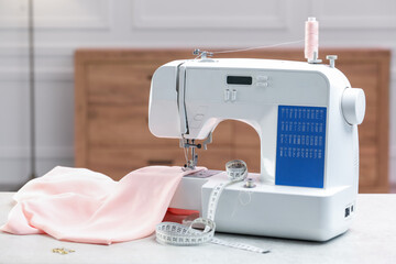Sewing machine with threads, measuring tape and fabric on white table in workshop