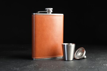 Hip flask, cup and funnel on black table