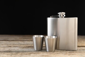 Hip flask and cups on wooden table, space for text
