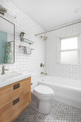 A bathroom with a natural wood floating cabinet, white marble countertop, marble hexagon tile flooring, and a subway tile shower.