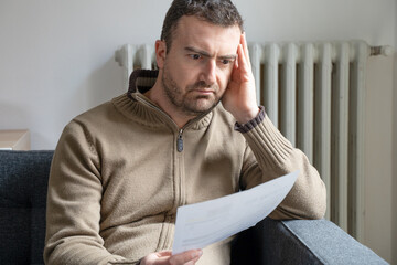 Shocked man reading some bills energy expenses on sofa living room