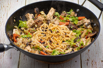 Mushroom, tofu, daikon and carrot stirfry along with udon noodles, cast iron wok, wooden table