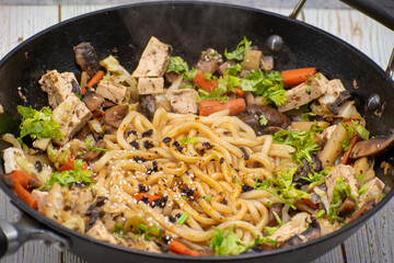 Mushroom, tofu, daikon and carrot stirfry along with udon noodles, cast iron wok, wooden table