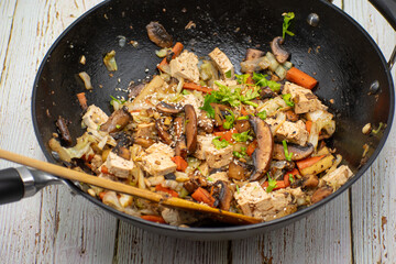 Mushroom, tofu, daikon and carrot stirfry along with udon noodles, cast iron wok, wooden table