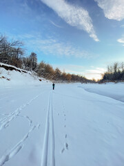 A person is leisurely walking down a snow covered road, enjoying the serene beauty of winter and the glistening white landscape all around them, taking in the crisp, cold air