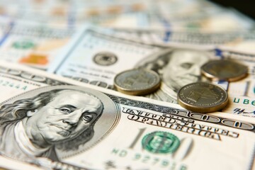 Close up of coins placed on a stack of one hundred dollar bills, highlighting financial concepts