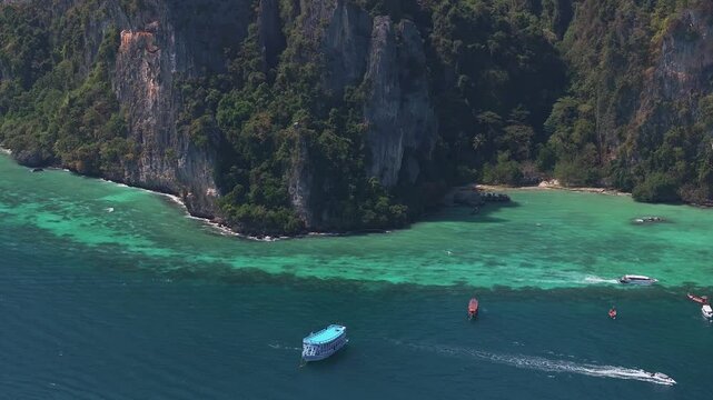 Aerial view of Phi Phi Island in Thailand, featuring turquoise waters, lush green cliffs, and boats on the deep blue sea creating dynamic movement.
