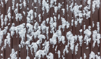 Fragment of a brown metal fence with white snow flakes stuck to it. Background. Texture. Close-up.