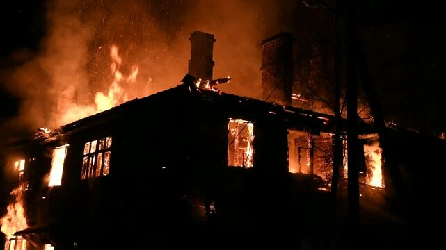 House is on fire at night, flames inside at home, burning window. The wooden building is ablaze, completely engulfed in fire. Loss of housing, disaster, trouble for unhappy people.