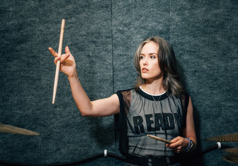 Female drummer practicing in small rehearsal studio, holding drumsticks, exuding passion, energy,...
