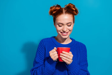 Cheerful young woman holding a red mug, wearing a cozy blue sweater on a vibrant background