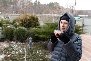 Woman with the cup of tea in winter. The woman enjoys hot tea in a home garden. The woman is...