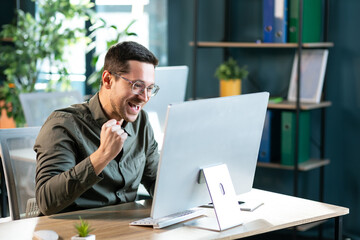 Naklejka premium Excited worker sitting at desk in coworking space use computer reading message looking at device screen received great unbelievable opportunity or reward. Motivated employee celebrating job promotion