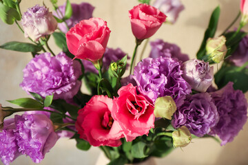 Vase with beautiful eustoma flowers near beige wall, closeup