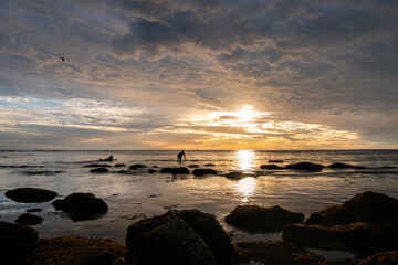 Sunset on the beach, with beautiful clouds and silhouettes of humans ready to surf in Southern California