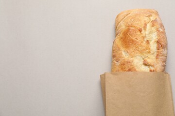 Paper bag with fresh baguette on light gray table, top view. Space for text