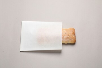 Paper bag with fresh ciabatta on beige background, top view