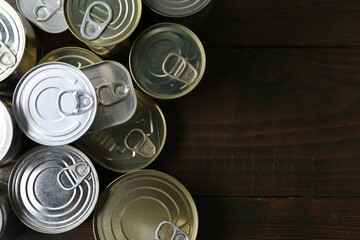 Many closed tin cans on wooden table, flat lay. Space for text