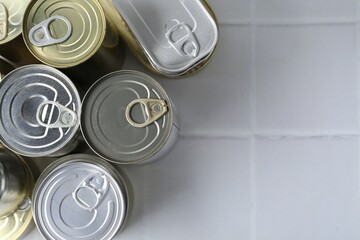 Many closed tin cans on white tiled table, flat lay. Space for text