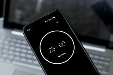 A phone with a black and white 25-minute timer to study with pomodoro method on laptop keyboard, study business background