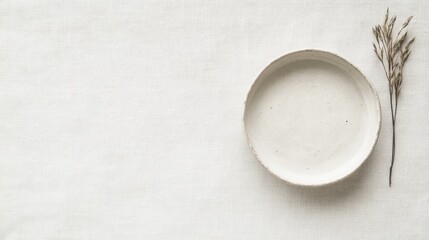 Empty ceramic plate and dried plant on linen fabric.