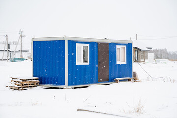 Naklejka premium A vibrant blue container house is prominently situated right in the middle of a vast snowy field, surrounded by the beautiful winter landscape and crystalclear ice formations