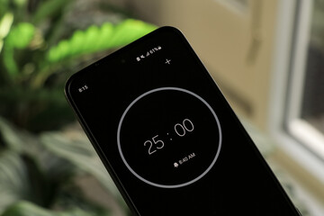 A phone with a black and white 25-minute timer to study with the pomodoro method on a blurry plants background