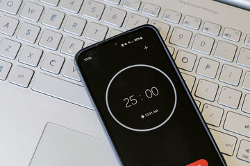 A phone with a black and white 25-minute timer to study with pomodoro method on laptop keyboard,...