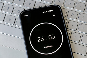 A phone with a black and white 25-minute timer to study with pomodoro method on laptop keyboard,...