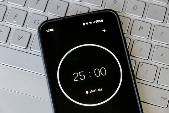 A phone with a black and white 25-minute timer to study with pomodoro method on laptop keyboard, study business background - Powered by Adobe