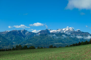 Fototapeta premium Lush green alpine pasture with scenic view of snow-capped mountain peaks of Karawanks seen from St Kathrein, Schiefling am See, Carinthia, Austria. Idyllic serene landscape in Austrian Alps in spring