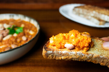 A warm and hearty legume soup served in a rustic ceramic bowl, topped with white and borlotti beans, garnished with fresh parsley, eaten with a slide of bread. Homely vibe, winter comfort food