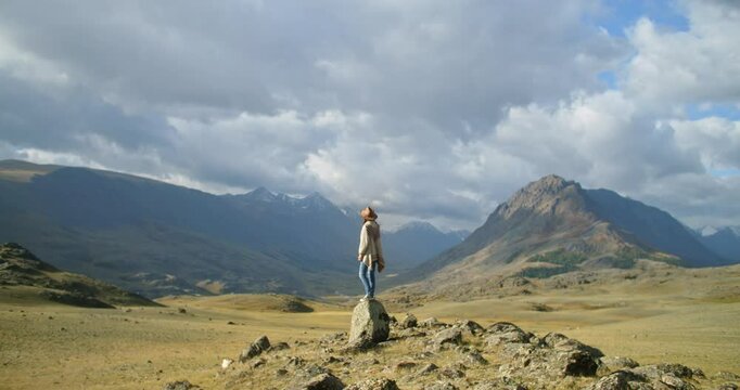 Female tourist standing on a rock enjoying the beautiful view of the altai mountains on a cloudy day with snow-capped peaks in the background