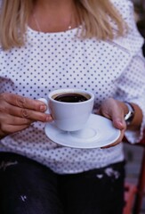 Young Woman Holding Coffee Cup Outdoors in Stylish Polka Dot Blouse