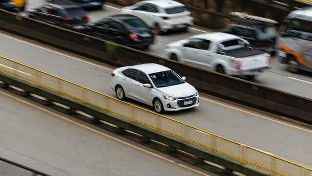 Panning shot of a white Chevrolet Onix Plus on a busy highway, Aerial view of a modern compact sedan in motion

