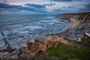 Green cactus on orange cliff in lowlight with panoramic view to São Sebastião beach in the evening, Ericeira - Mafra PORTUGAL