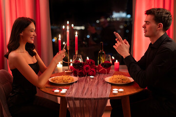 Online dating app. Young man and woman using mobile phones during romantic dinner date in restaurant, sitting at table and ignoring each other